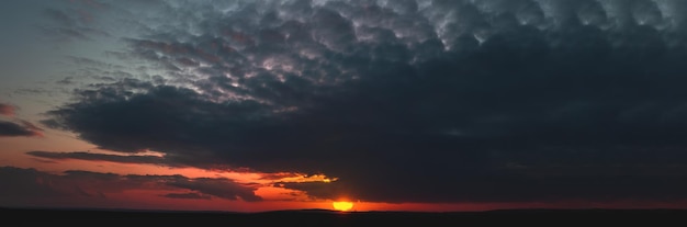 Puesta de sol oscura con nubes sombrías y luz roja en el horizonte