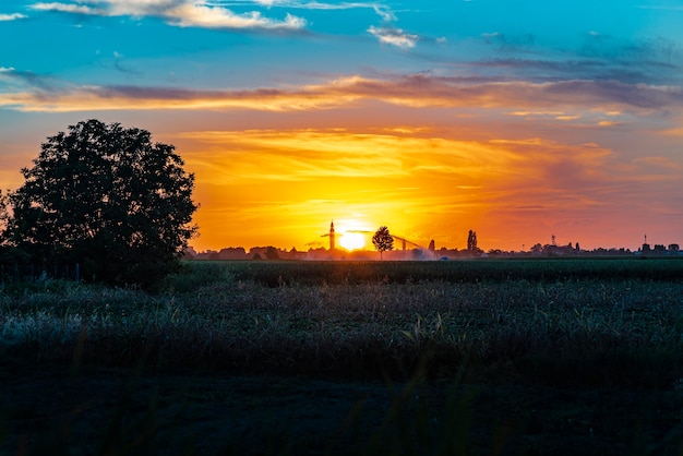 Puesta de sol en un paisaje con campanario, árboles y campo