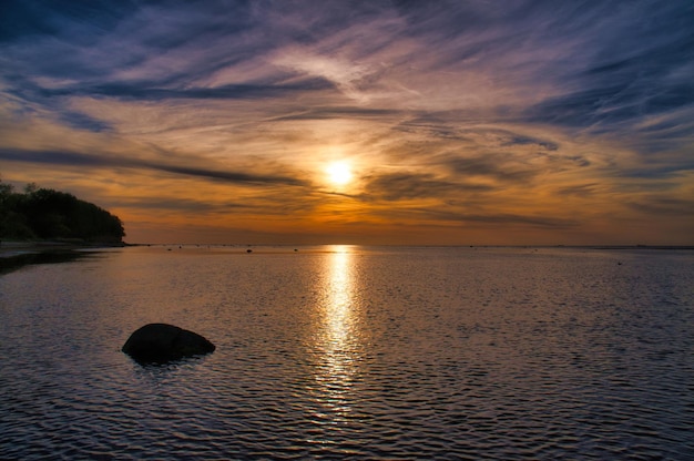 Puesta de sol pequeñas rocas en el agua en la orilla Ondas de luz En el Mar Báltico