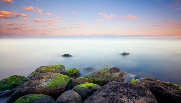 Puesta de sol en las piedras del mar en la orilla Increíble puesta de sol de ensueño rosa perfecta Agua suave