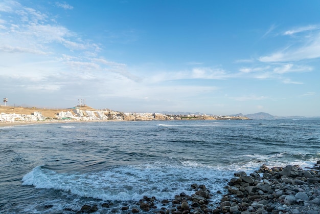 Puesta de sol en la playa con cielo azul y mar y nubes blancas. Embarcadero de roca. Punta Hermosa, Lima.