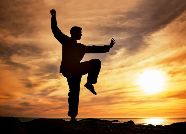 Puesta de sol en la playa y la silueta del hombre haciendo yoga para el cuerpo mental y el bienestar espiritual en la noche Crepúsculo pilates y la sombra del hombre haciendo ejercicio de meditación para la salud en la naturaleza junto al agua del océano