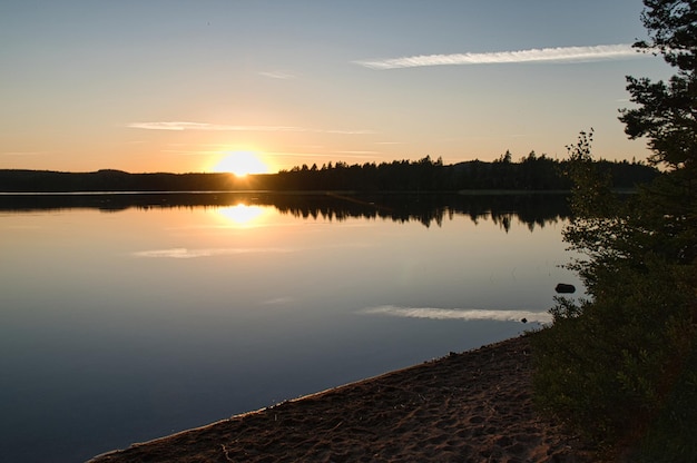 La puesta de sol con reflejo en un lago sueco en Smalland con arbustos en primer plano en la orilla