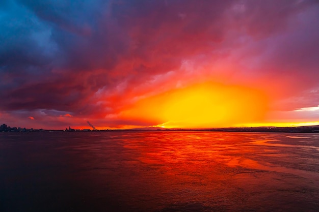 Puesta del sol roja y azul colorida en la bahía del mar en la oscuridad y la ciudad en la distancia