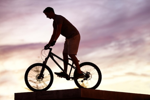 Puesta de sol de silueta y ciclismo con hombre en bicicleta para deportes de aventura y fitness Ejercicio de acción y salud con ciclista masculino montando en bicicleta bmx para un viaje urbano o neutral en carbono con maqueta