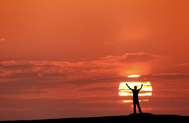 Foto puesta de sol con la silueta de un hombre con los brazos levantados