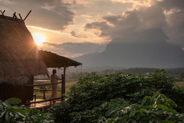 Puesta de sol sobre la cabaña de madera y la mujer asiática disfrutando de la vista de la montaña Doi Luang Chiang Dao en las tierras altas de Chiang Dao, Chiang Mai, Tailandia