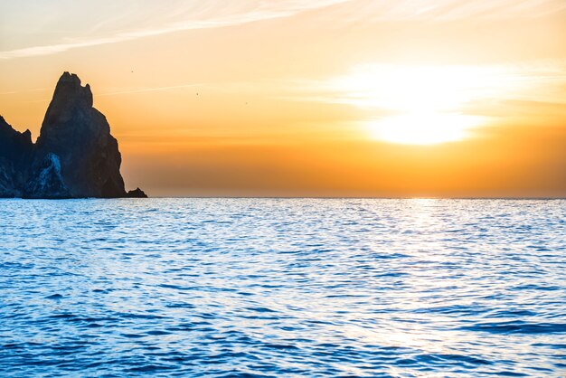 Puesta de sol sobre el mar azul con rocas y cielo naranja