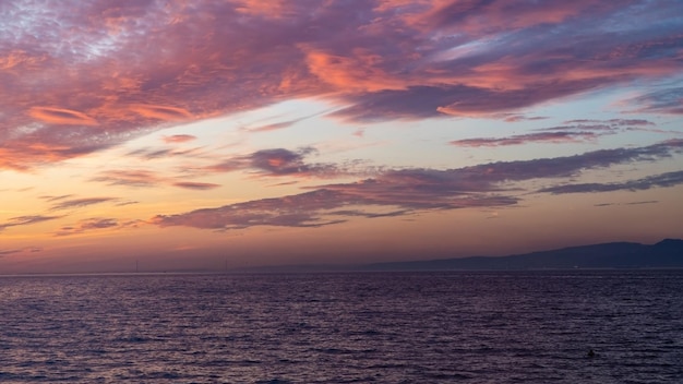 Una puesta de sol sobre el océano con un cielo rosa y algunas nubes.