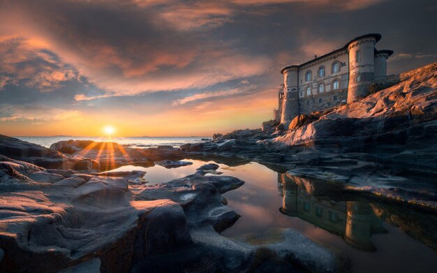 una puesta de sol sobre una playa rocosa con una puesta de Sol en el fondo