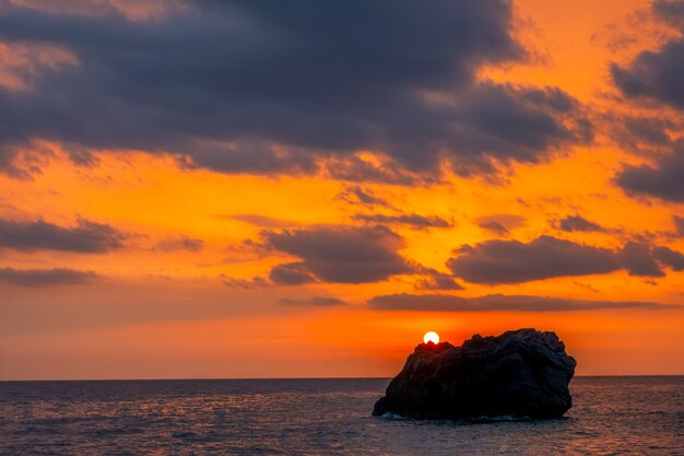 Puesta de sol sobre una roca solitaria en un mar en calma. Colores asombrosos en el cielo nublado