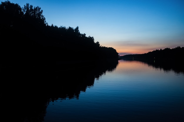 Puesta de sol y su reflejo en la superficie del agua del río Colores brillantes y siluetas de árboles