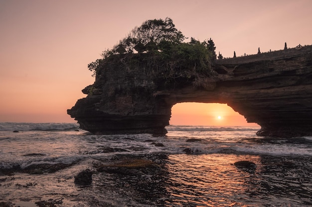 Puesta de sol a través de un acantilado rocoso en la orilla del mar al atardecer Pura Batu Bolong Bali