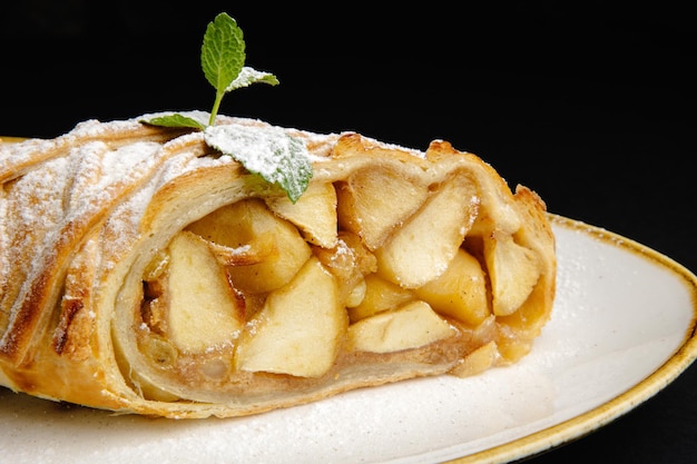 Puffgebäck mit Apfelstrudel mit Zuckerpulver und Minze an der Spitze, isoliert auf schwarzem Hintergrund