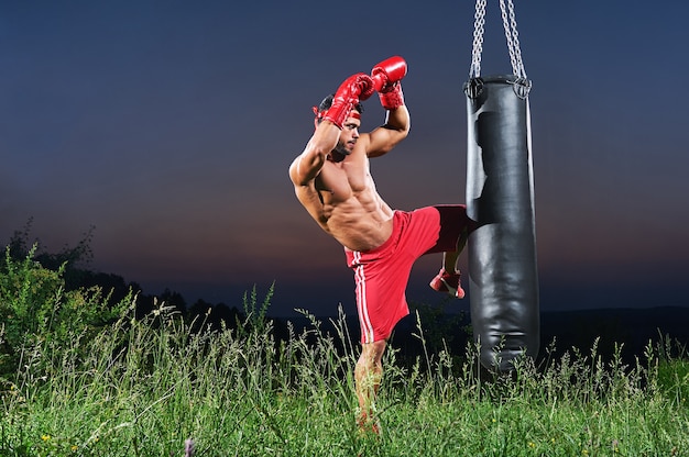 Pugilista masculino considerável novo que pratica em um saco de perfuração fora