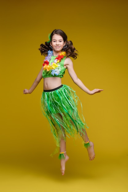 Pulando engraçadinha em roupas brilhantes de verão com emoção positiva posando na parede amarela