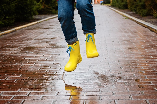 Pulando na poça Pernas femininas em botas de borracha amarelas pulando na poça Jovem despreocupada em saltos de botas de chuva