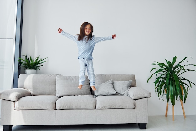 Foto pulando no sofá menina bonitinha dentro de casa sozinha criança aproveitando o fim de semana