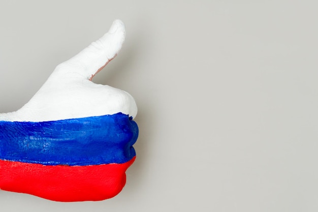 Foto pulgar arriba mano a mano con el dibujo de una bandera de rusia sobre un fondo gris