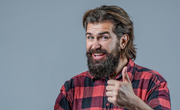 Los pulgares hacia arriba como el hombre barbudo con camisa a cuadros gesto positivo con los pulgares de la mano hacia arriba sonriendo