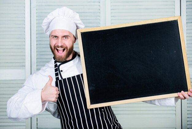 Pulgares arriba para nuestra escuela de catering Maestro cocinero dando clases de cocina Jefe de cocina enseñando clases magistrales en la escuela de cocina Educación de cocina y preparación de alimentos Hombre sosteniendo espacio de copia de pizarra