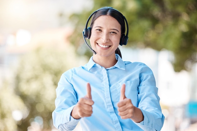 Pulgares arriba servicio al cliente y mujer feliz de pie afuera con un auricular y una actitud positiva y amistosa Retrato de CRM telemarketing y operador de centro de llamadas mostrando apoyo y gracias