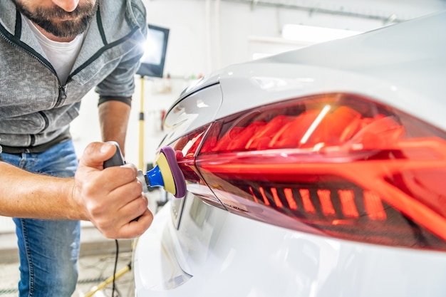 Pulido manual de faros de automóviles de lujo con la aplicación de equipos de protección.