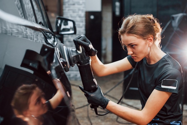 Pulido de la superficie del vehículo El automóvil negro moderno es limpiado por una mujer dentro de la estación de lavado de autos