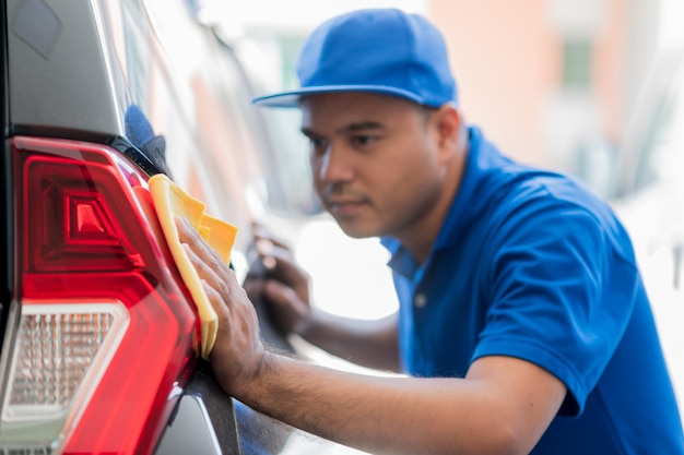 El pulidor de autos usa un paño de microfibra y un abrillantador para limpiar las luces traseras del auto y hacerlas brillar. Él cuida cada detalle del auto.