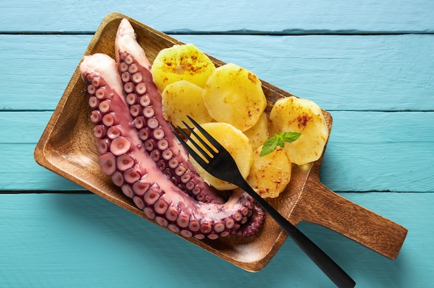 Pulpo cocido con patatas, en tablero para servir, superficie de madera azul, vista superior