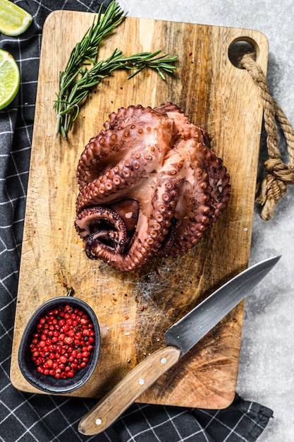 Pulpo entero hervido en una tabla de cortar lista para cortar. Superficie gris. Vista superior