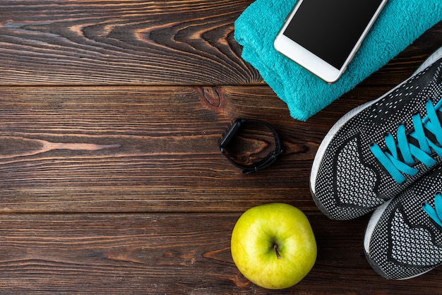 Pulseira de fitness, tênis, celular e garrafa de água em madeira escura