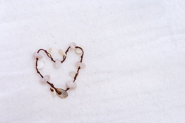 Pulsera de concha en forma de corazón sobre arena blanca y fina