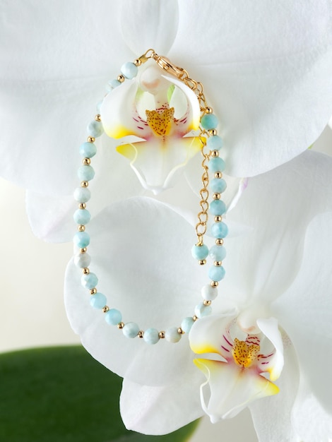 Foto pulsera dorada con gemas turquesas en flor de orquídea blanca.