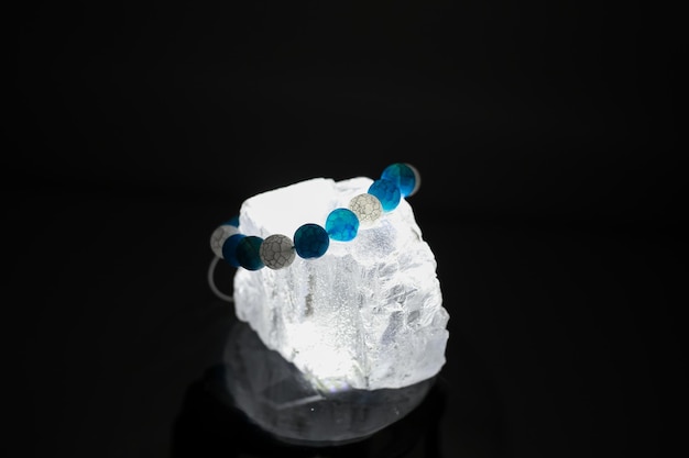 Una pulsera hecha de piedras naturales de diferentes colores se encuentra sobre una gran piedra transparente