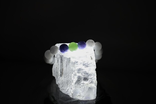 Una pulsera hecha de piedras naturales de diferentes colores se encuentra sobre una gran piedra transparente