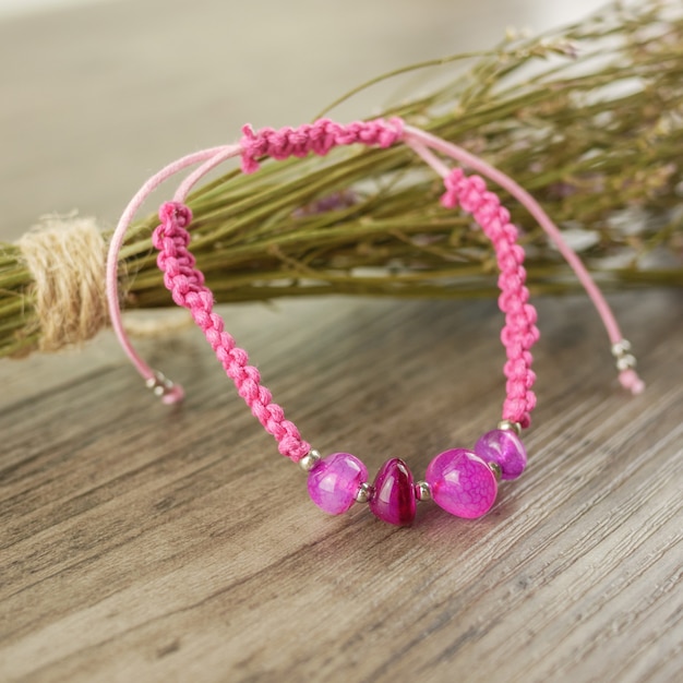 Pulsera rosa y flor seca en mesa de madera.