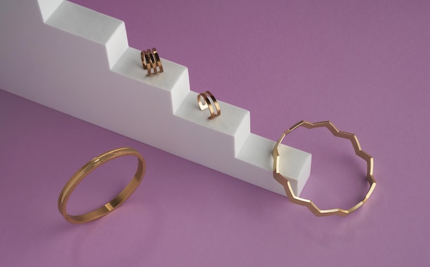 Pulseras y anillos dorados de diseño moderno en el podio de las escaleras sobre fondo púrpura con espacio para copiar