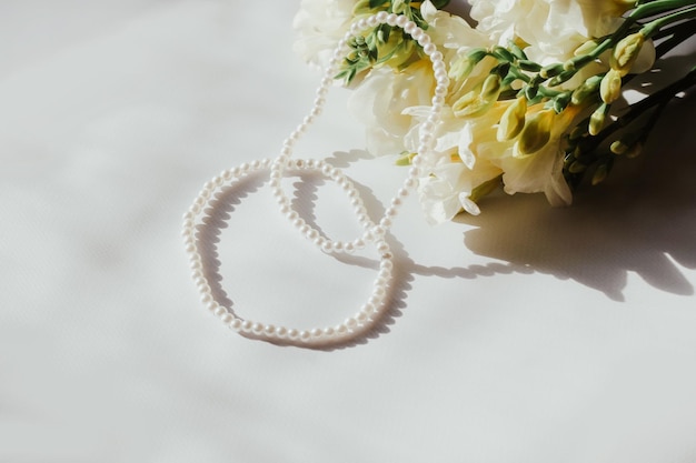 Pulseras blancas con perlas sobre un fondo blanco con flores.