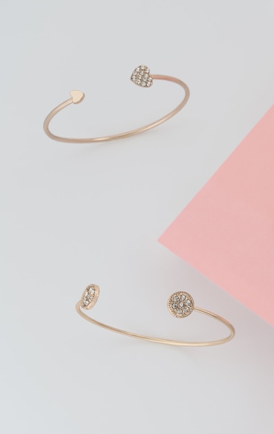 Pulseras doradas con brillantes sobre fondo rosa y blanco