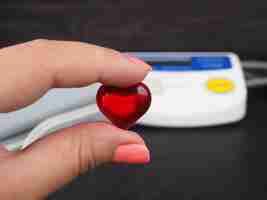 Foto pulsímetro en el escritorio del médico para el diagnóstico de la superficie negra de la enfermedad cardíaca, un manguito de presión arterial y un pequeño corazón en la mano, vista superior del tonómetro