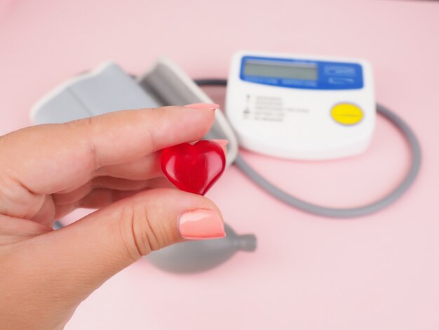 Foto pulsímetro en el escritorio del médico para el diagnóstico de la superficie negra de la enfermedad cardíaca, un manguito de presión arterial y un pequeño corazón en la mano, vista superior del tonómetro