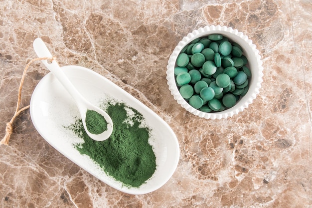 Pulver- und Spirulina-Tabletten in Schalen auf einem Marmortisch Draufsicht Superfood-Nahrungsergänzungsmittelquelle für Vitaminprotein und Betakarotin