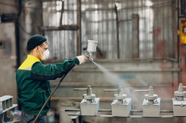 Pulvergrundierung von Metallteilen. Arbeiter in einem Schutzanzug sprüht Pulverfarbe aus der Waffe auf die Konstruktion von Metallprodukten im Werk