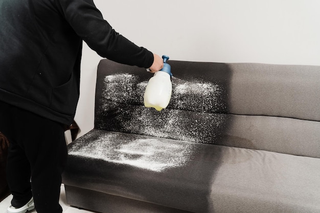 Pulverização de detergente no sofá para limpeza a seco usando máquina extratora Processo de limpeza a seco para remoção de manchas e sujeira do sofá em casa Serviço de limpeza profissional