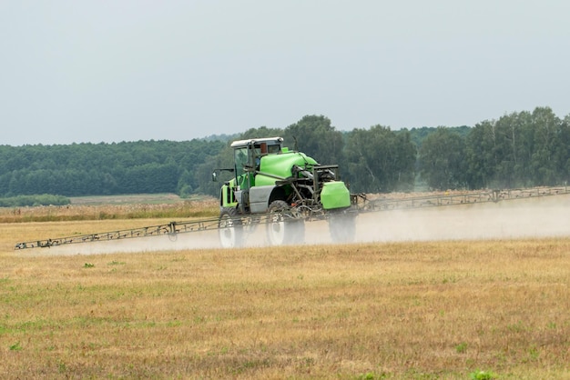 Foto pulverizador automotor trabalha no campo em um dia quente e ensolarado controle de ervas daninhas com pesticidas e produtos químicos o trator usa um pulverizador para pulverizar fertilizantes líquidos no campo