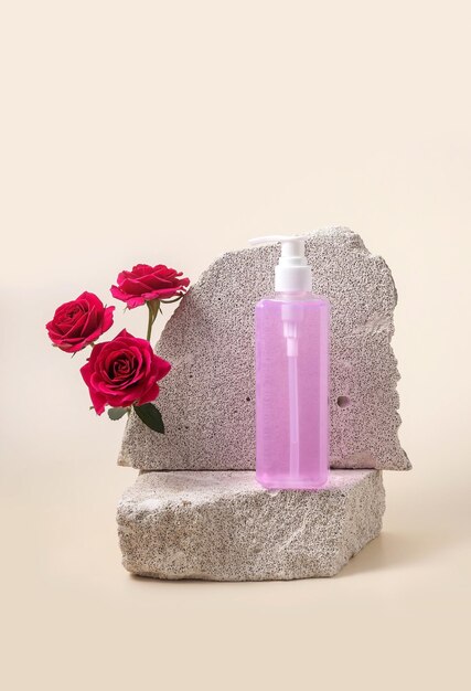 Foto pumpenflasche für kosmetika auf dem podium aus stein und rosen auf beigenem hintergrund