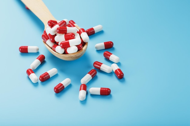 Un puñado de cápsulas de pastillas rojas y blancas en una cuchara de madera sobre un fondo azul. Primer plano del espacio libre Vista superior
