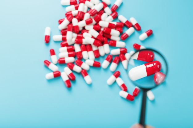 Un puñado de cápsulas de pastillas rojas y blancas se examinan con una lupa sobre un fondo azul.