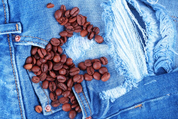 Puñado de granos de café sobre fondo de jeans rasgados